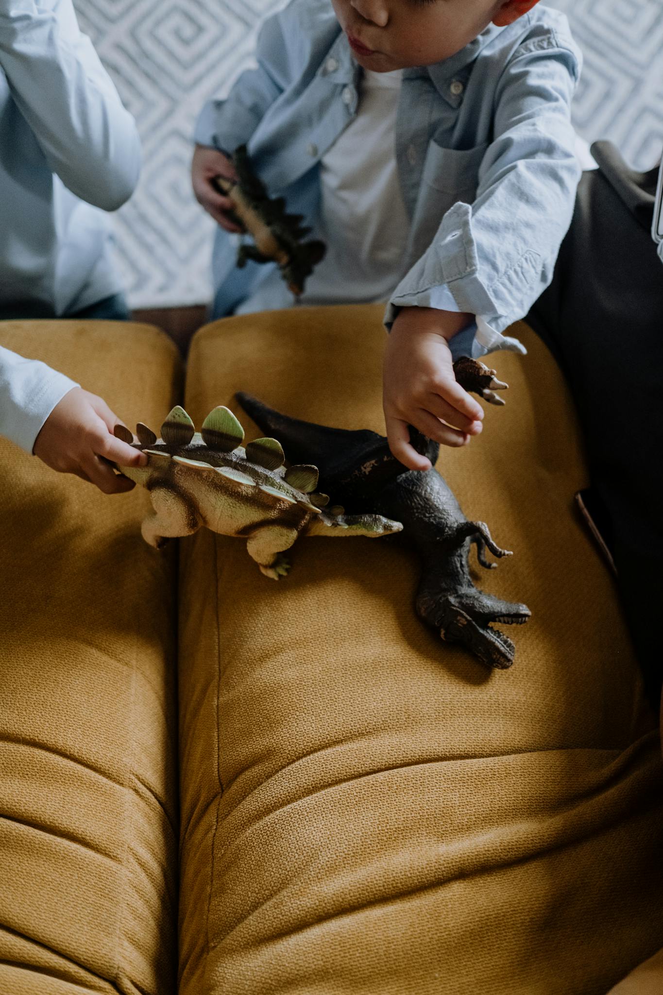 Kids engaged in imaginative play with dinosaur toys on a couch indoors.