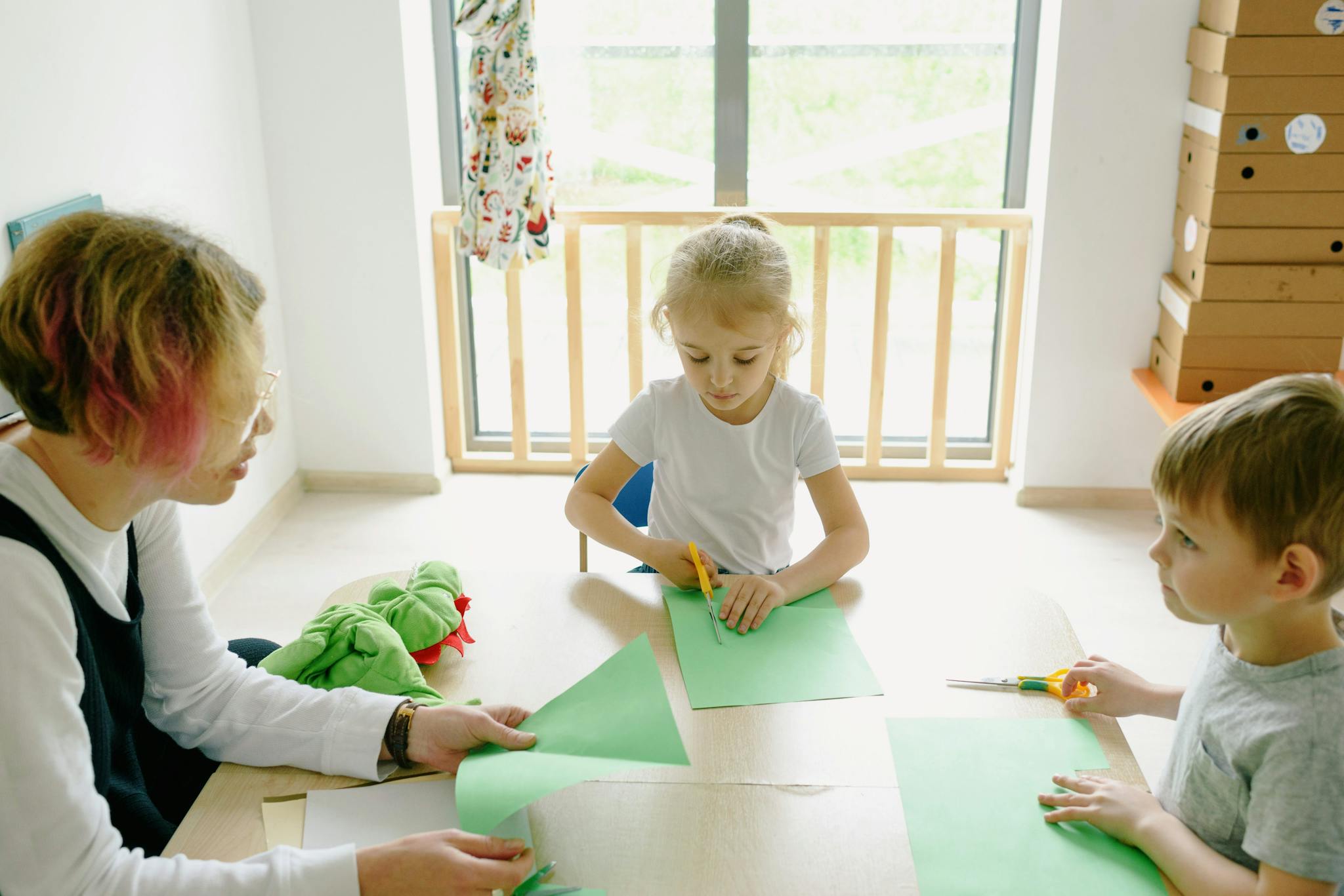Two children and an adult engaging in paper cutting activity at a table indoors.