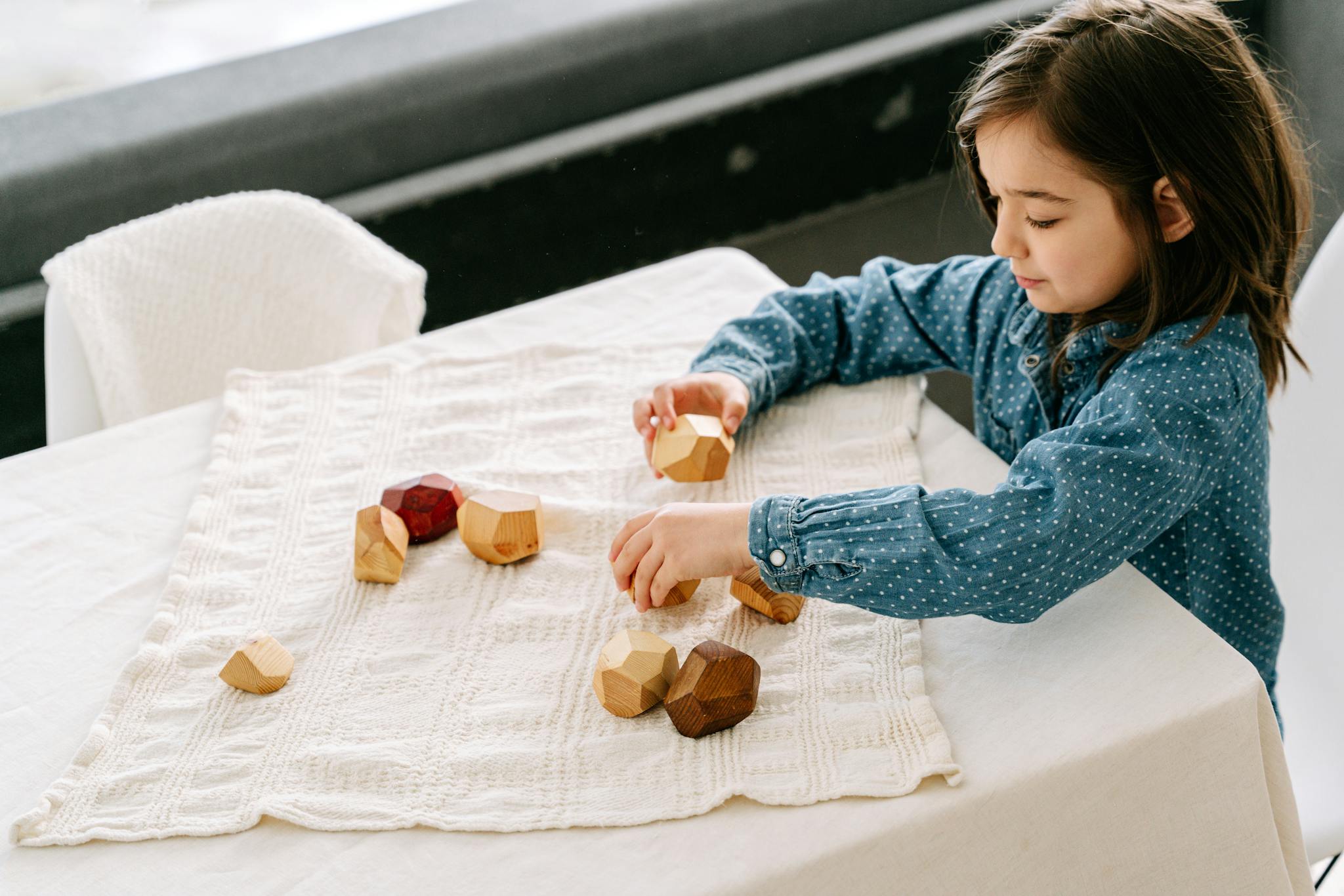Young girl playing with sustainable wooden blocks indoors, encouraging creativity and learning.